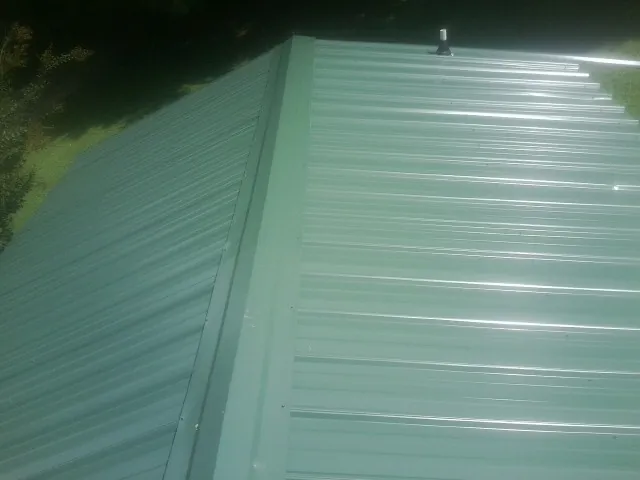 New green metal panels meeting at the ridge of a roof — Flat Roof Repair work by our crew in Roanoke