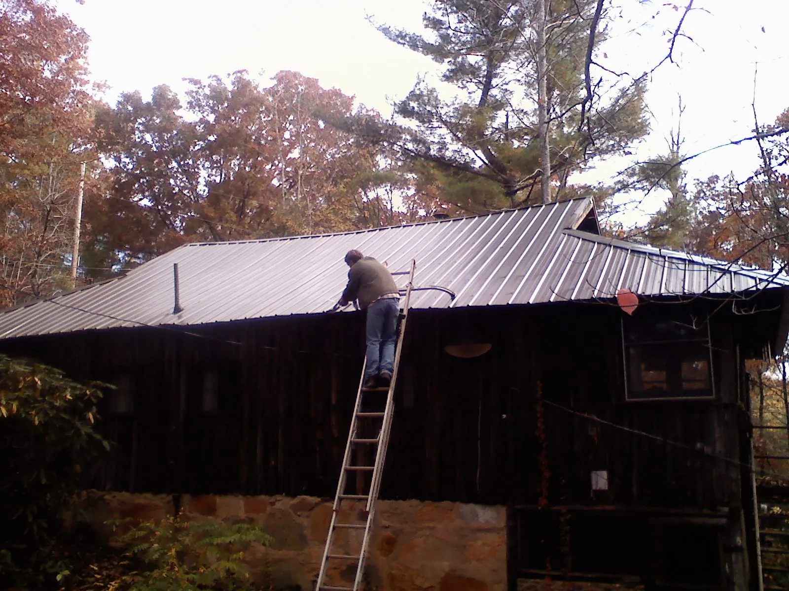 Roofer on a ladder working along the edge of a cabin metal roof in Roanoke